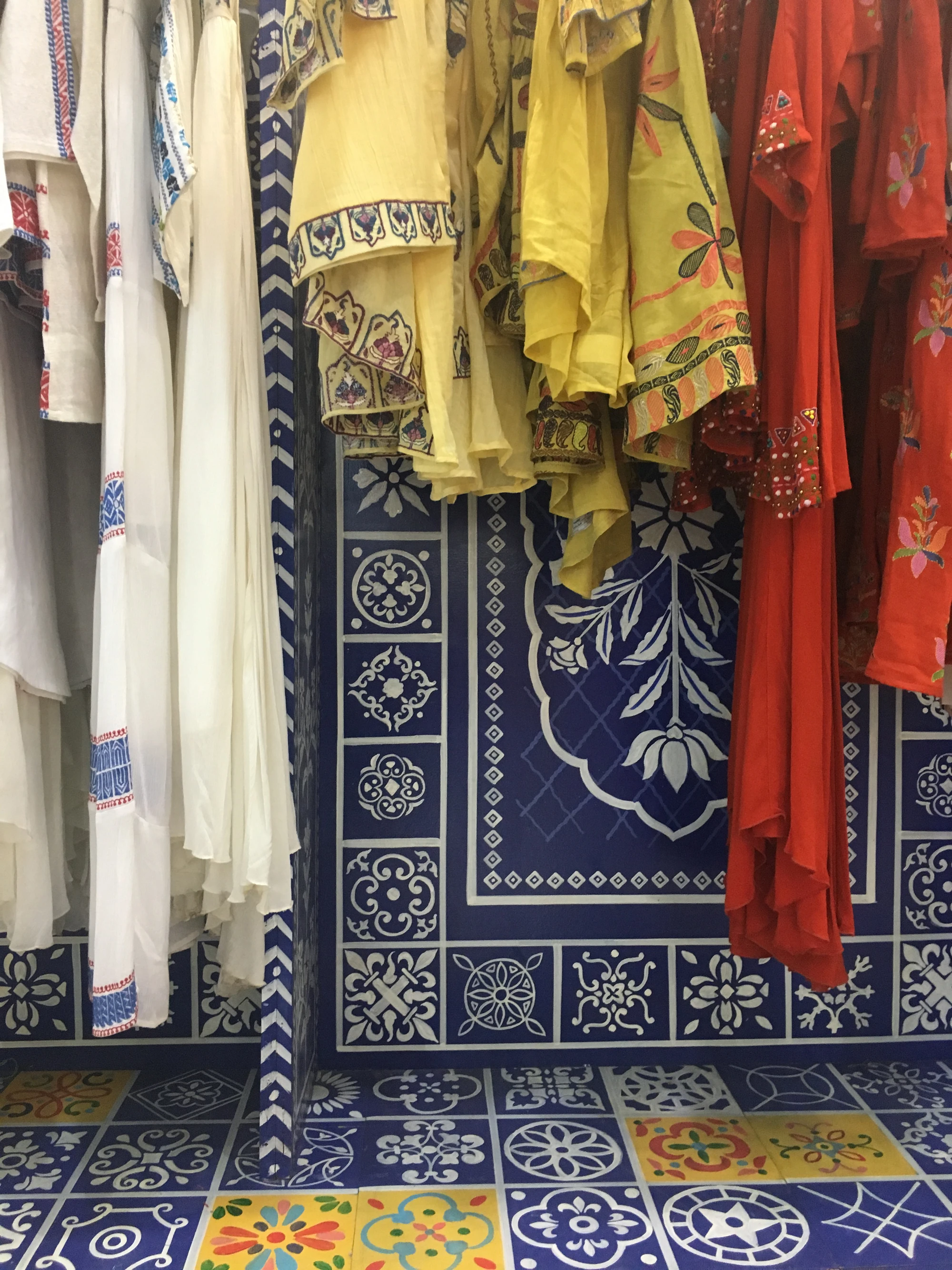 Colorful embroidered garments hanging against a blue Moroccan-tiled wall