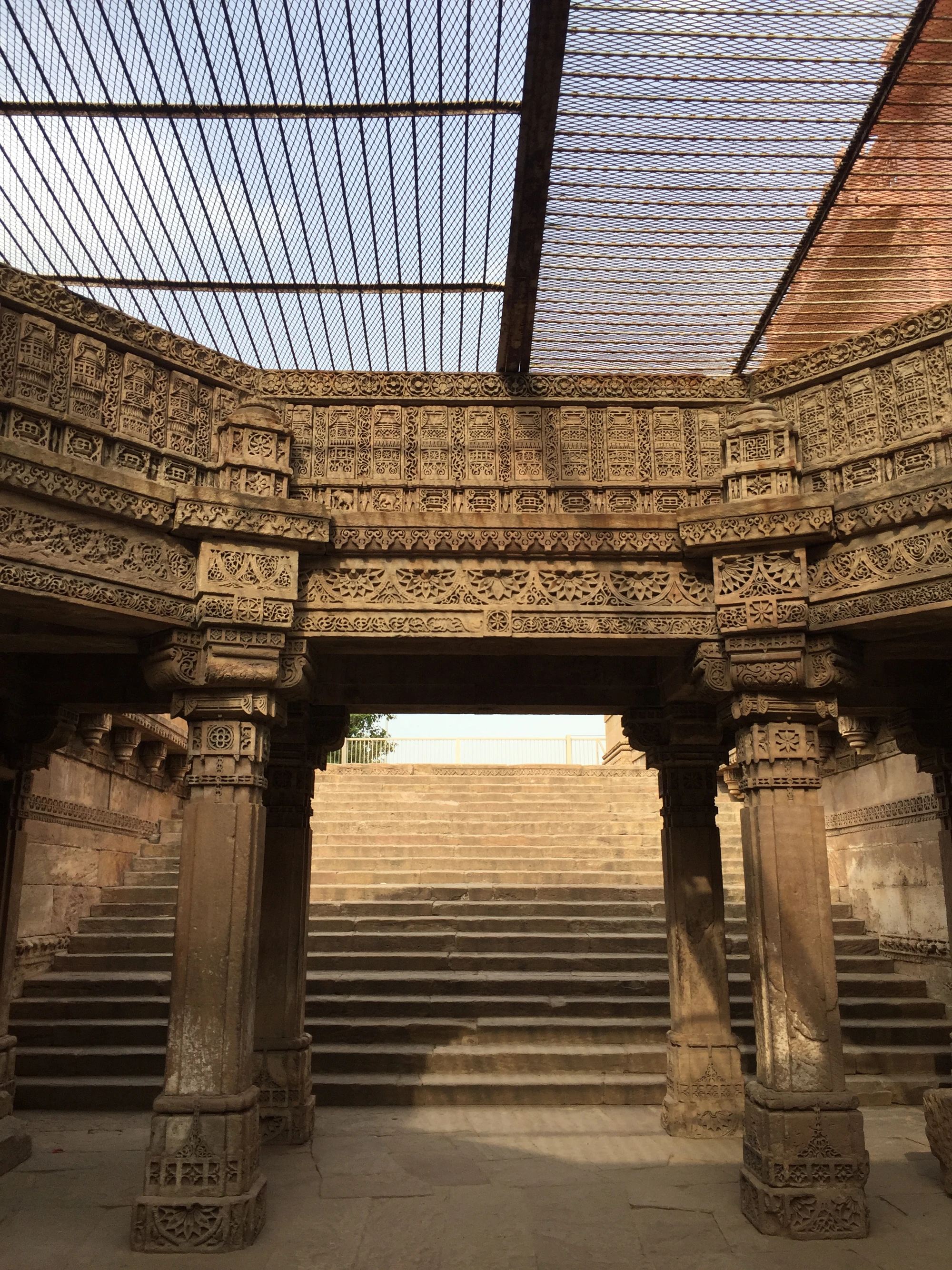 A carved stone stepwell archway under a wire-mesh sky