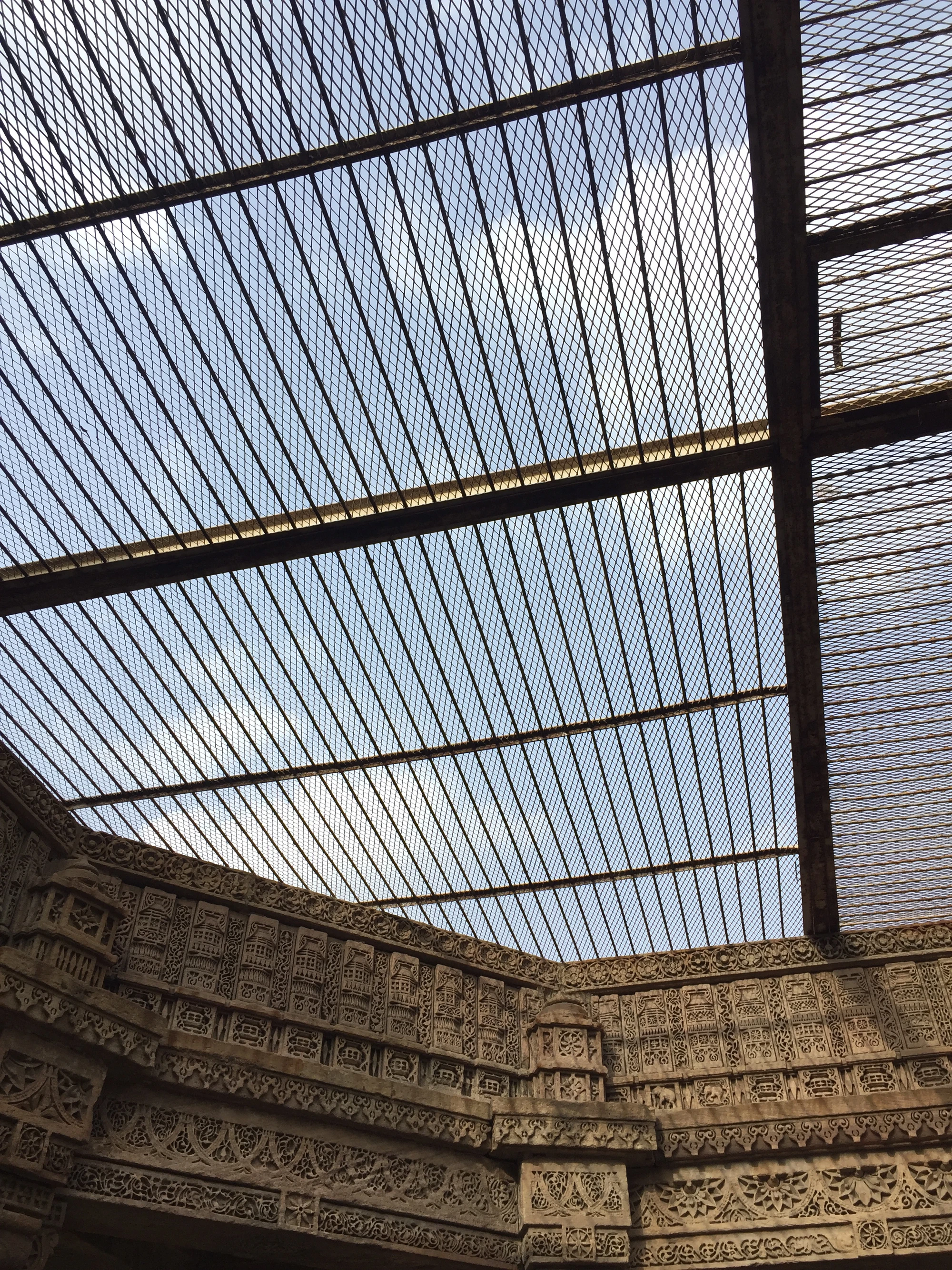 A wire-mesh ceiling over an intricately carved stepwell courtyard