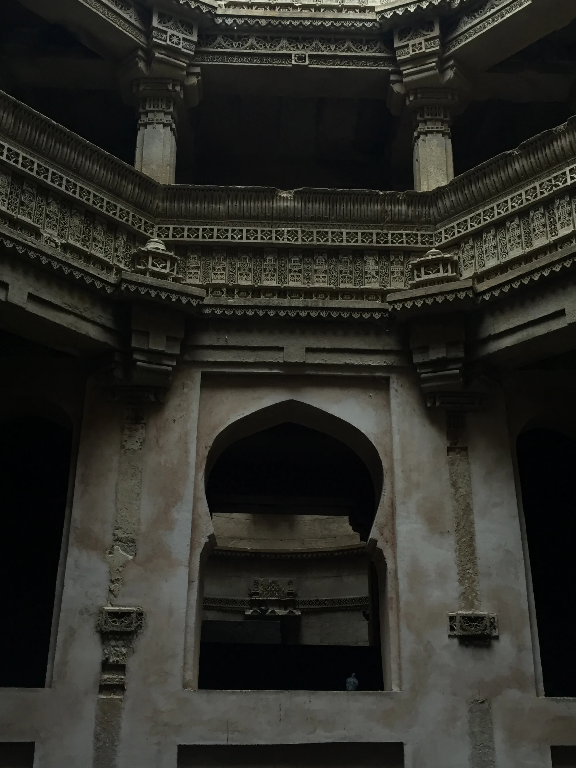 A dark stepwell interior with a pointed stone archway