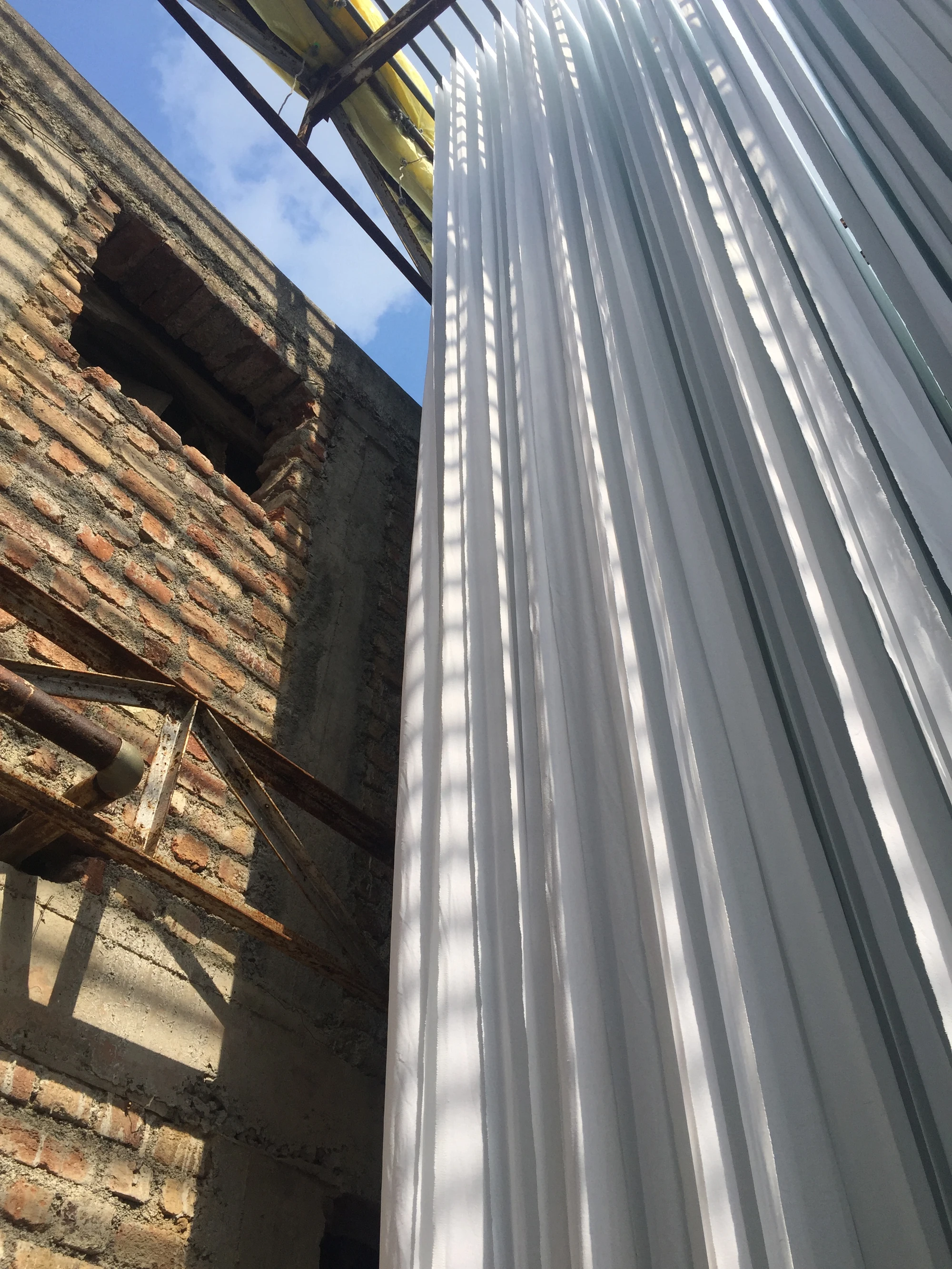 Pleated white fabric drying against a brick building under construction