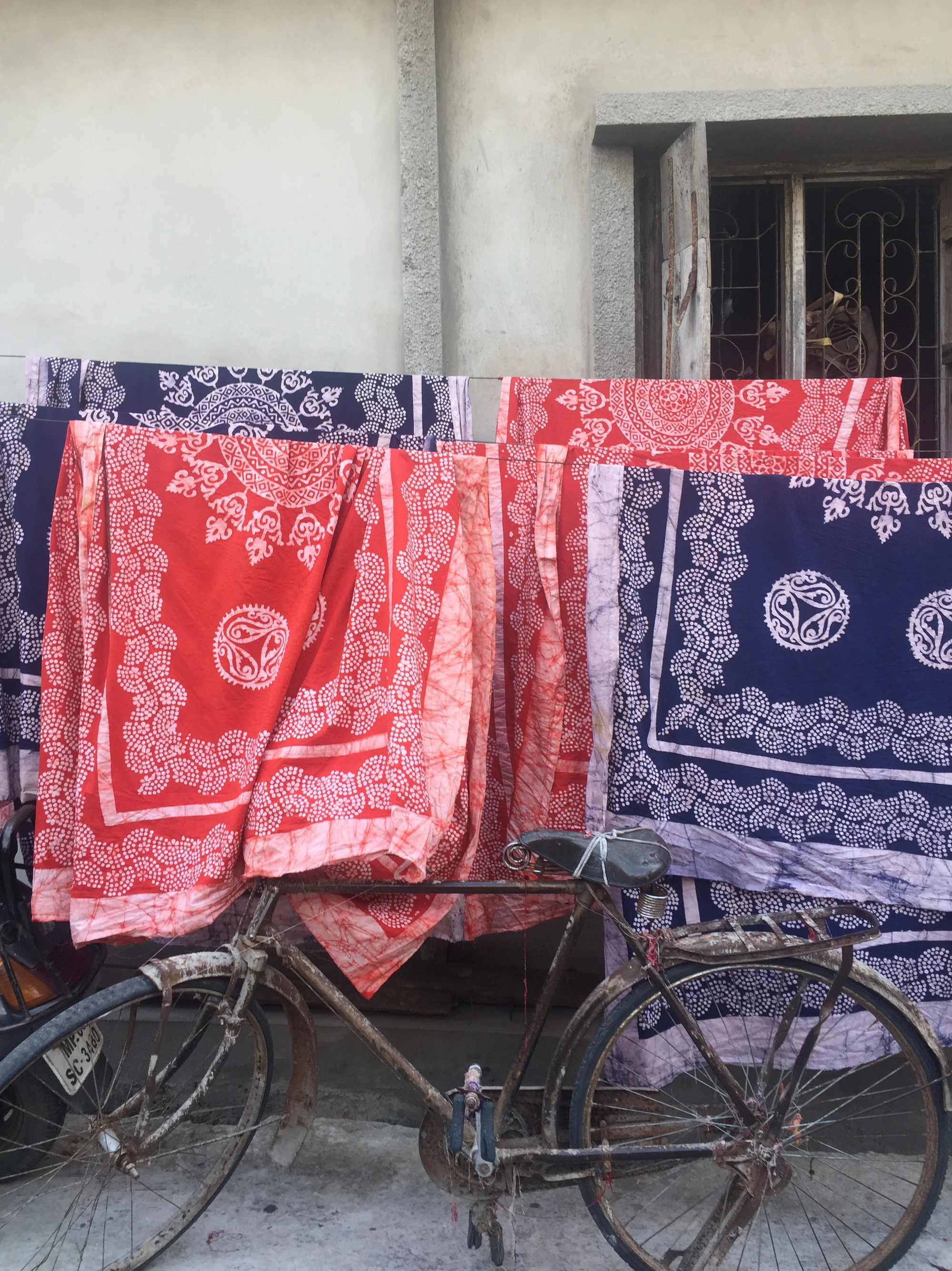 Red and indigo bandhani fabrics drying beside an old bicycle