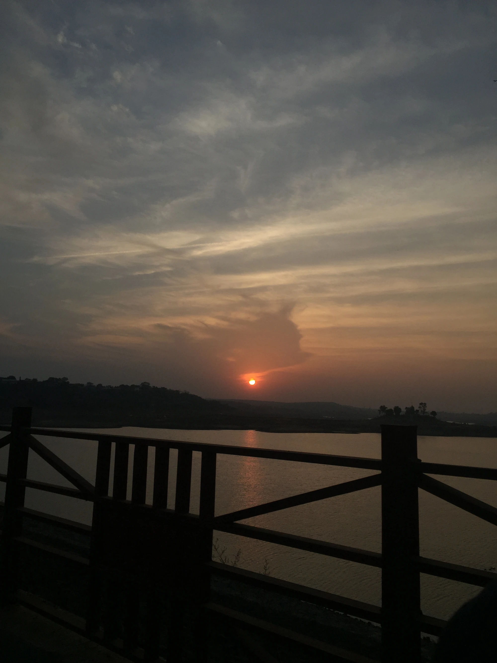 The sun setting over still water, seen through a railing