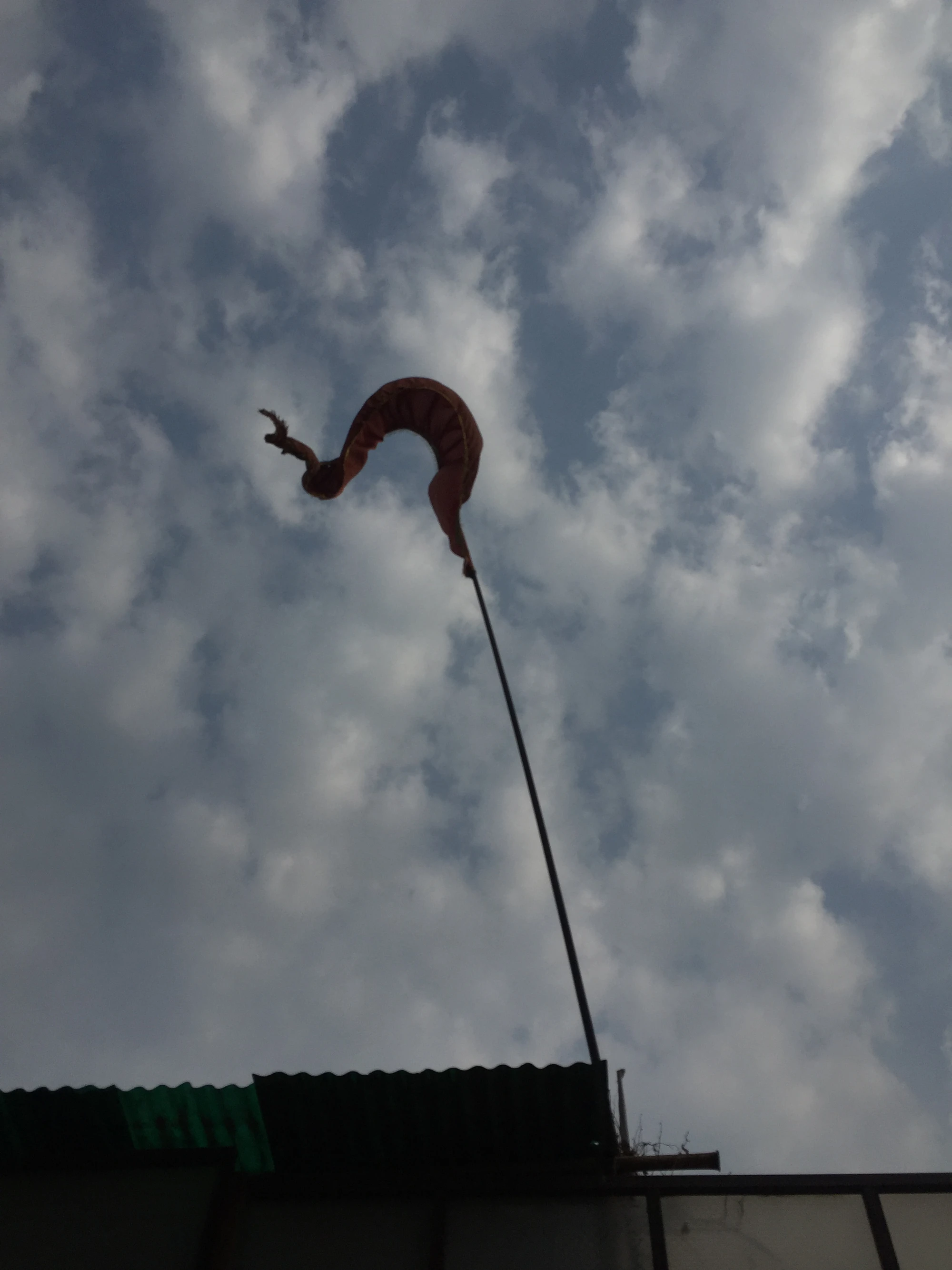 An orange flag curling in the wind against a cloudy sky