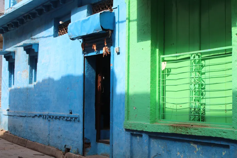 A blue and green painted building facade with barred windows