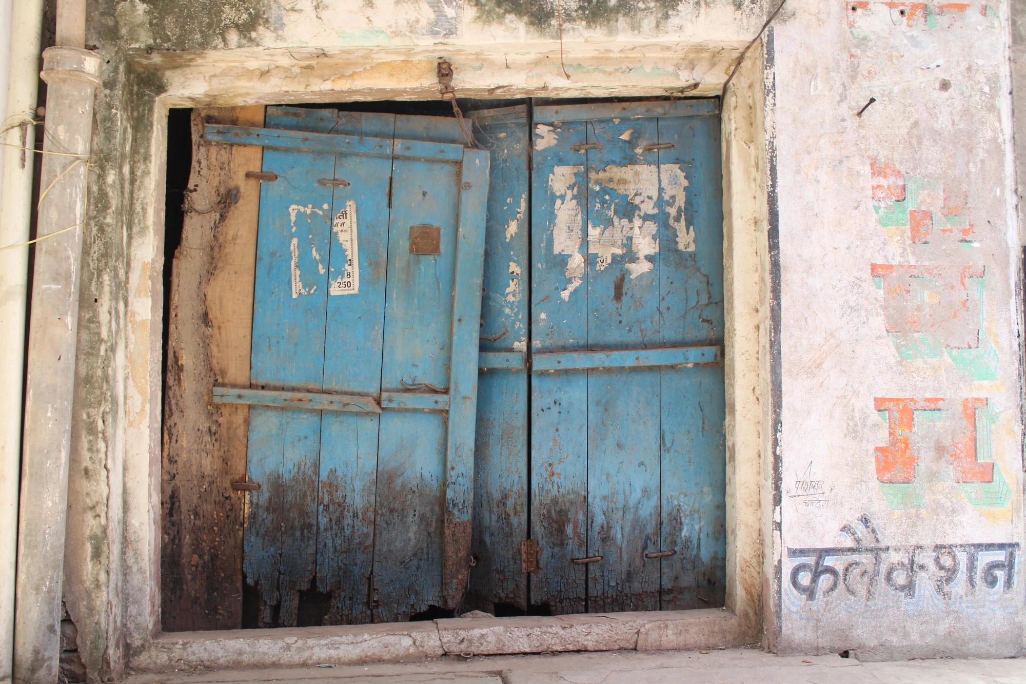 Weathered blue wooden doors on a whitewashed building with Hindi signage