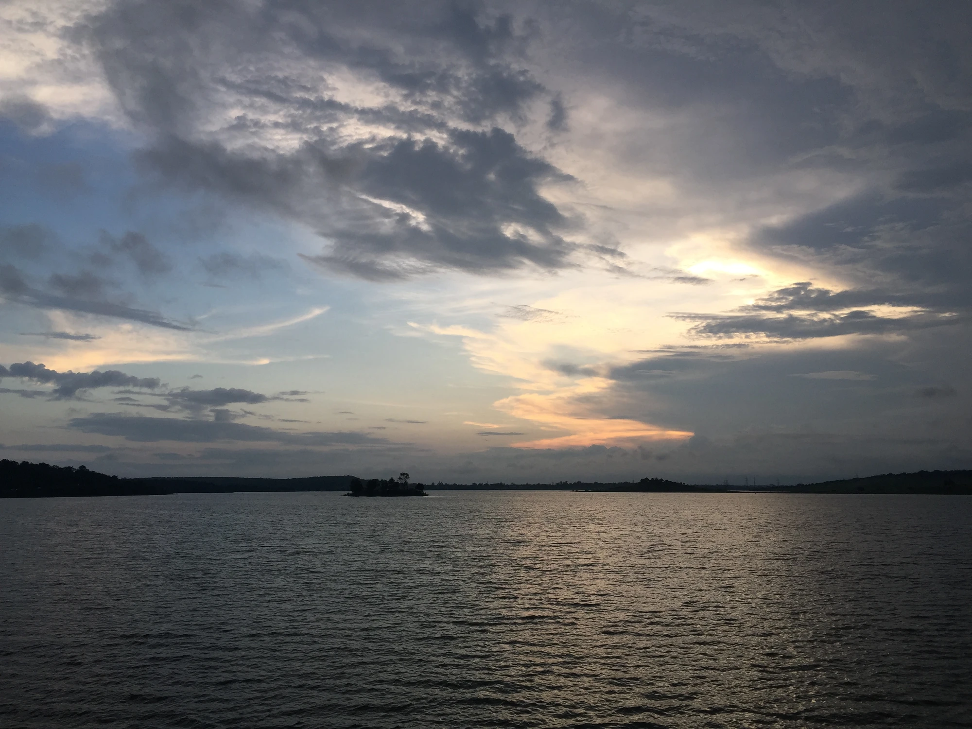 A calm lake at dusk with a small tree-covered island