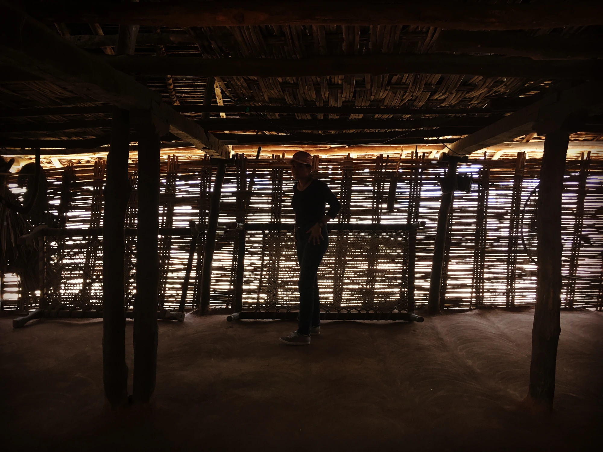 A weaver's silhouette inside a sunlit bamboo-walled workshop