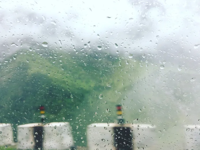 A rain-streaked window looking out over a green hillside