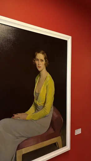 A portrait of a woman in a yellow cardigan on a red wall