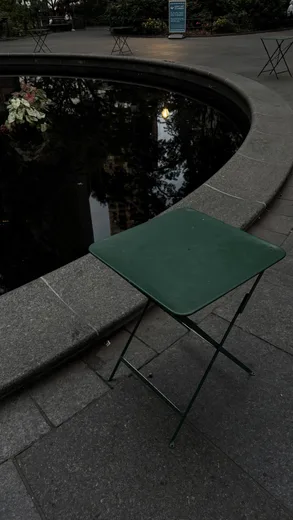 A green folding table beside a curved stone pool in a dark park