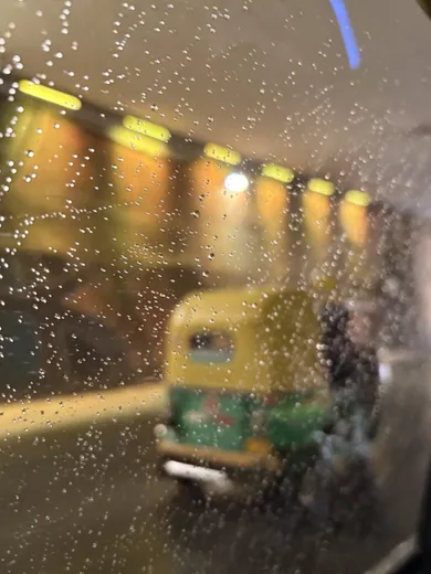 A yellow auto rickshaw seen through a rain-streaked window at night