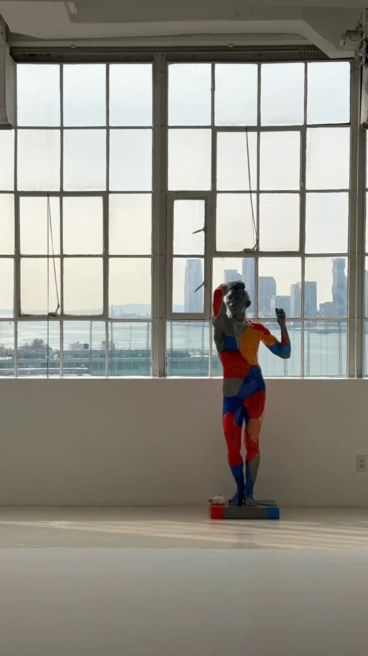 A colourful sculpture in front of tall studio windows with a view of the Hudson